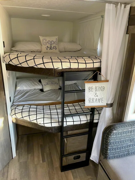 Step inside this RV rental's cozy bunk bed area, featuring checkered bedding & inspirational signs for a comfy stay.. Forest River Vibe 2021