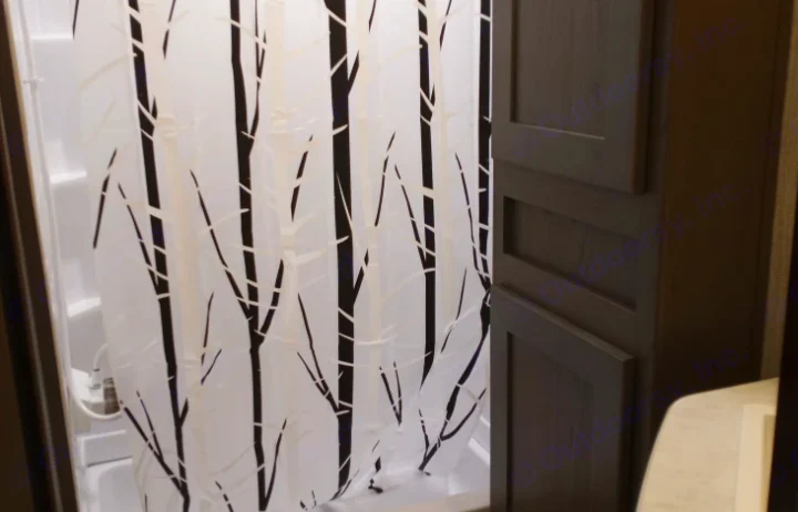 Compact RV rental bathroom: Black & white birch tree shower curtain & dark storage cabinets visible.. Cruiser RV MPG Ultra Lite 2021