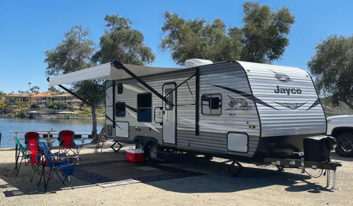 Enjoying the outdoors! This Jayco RV rental is set up at a scenic lakeside campsite with an extended awning and chairs.. Jayco Jay Flight 2021