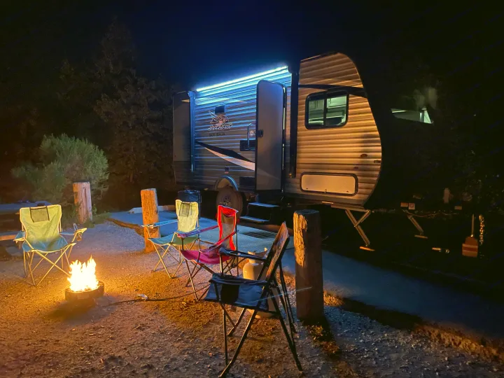 An RV rental illuminated by blue lights at night, with a cozy campfire and chairs set up for a relaxing evening.. Jayco Jay Flight 2021