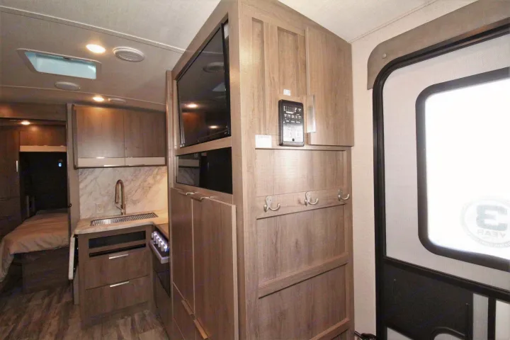 Interior of an RV rental with a functional kitchenette, entertainment center, and sleeping quarter in the background.. Grand Design 2400BH 2022