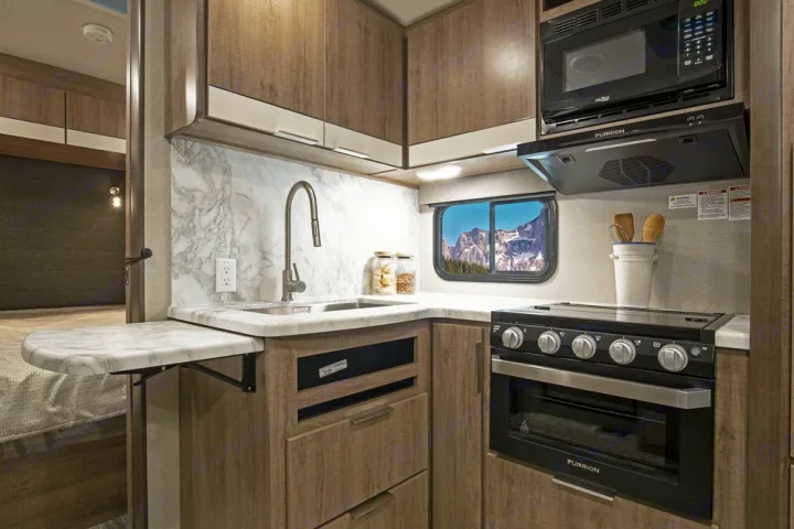 Functional RV rental kitchen with sink, stove, microwave, and clever extendable counter for extra space.. Grand Design 2400BH 2022