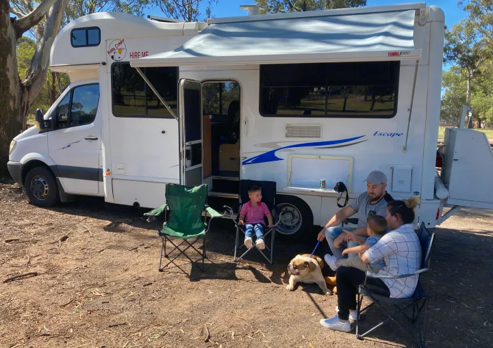 Family and their bulldog relax outside their white rv rental motorhome under an awning, enjoying a sunny day outdoors.. Mercedes Dreamseeker River 6 2008