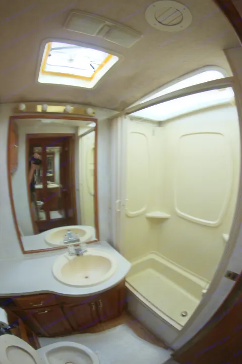 Inside an RV rental, this light-colored bathroom offers a sink, mirror, toilet, and a stand-up shower with a skylight.. Winnebago Adventurer 1999