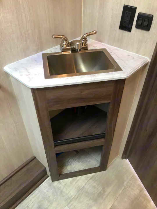 Modern RV rental bathroom features a compact corner sink vanity with a stainless steel basin and open shelving below.. Genesis Supreme Rv Genesis Supreme 2021