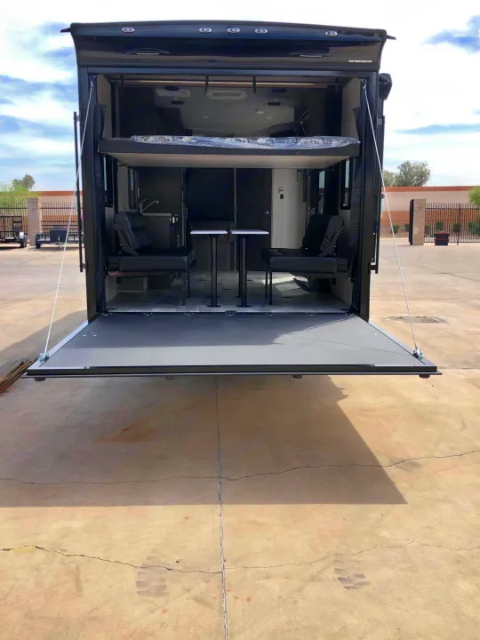 This RV rental's rear ramp opens to reveal a versatile interior with a bunk bed, seats, and tables, creating an outdoor deck.. Genesis Supreme Rv Genesis Supreme 2021