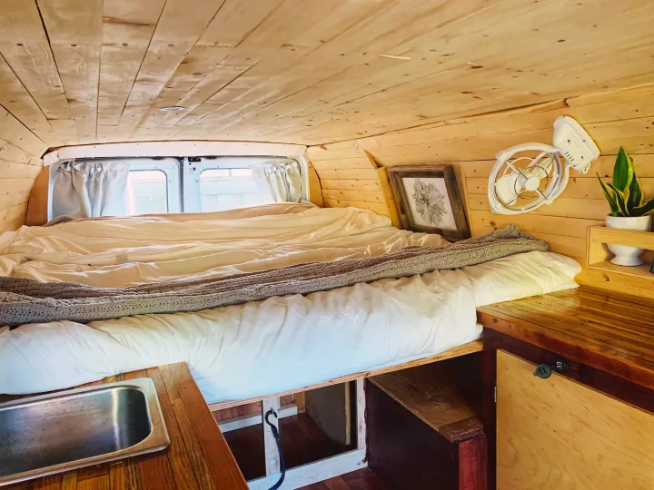 Cozy wooden RV rental interior: bed with white sheets, sink, fan, and plant, ready for adventures.. Ford Econoline E250supercab 2006