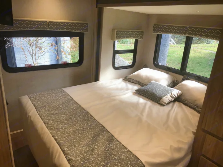 Bright RV rental bedroom: cozy bed, multiple windows with "EXIT" labels, and outdoor views. Great for travel.. Isata 3 2018