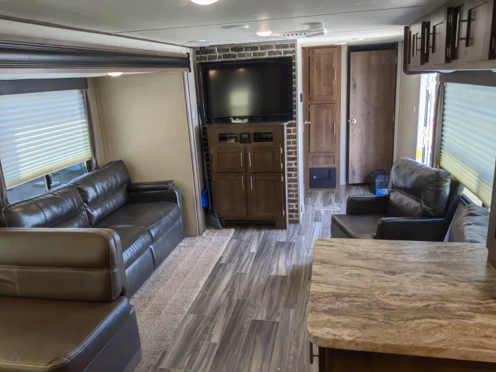 Spacious RV rental living area with dark leather sofas, TV on brick wall, wood-look floors. Ideal travel trailer interior for your journey.. Shasta Oasis 2019