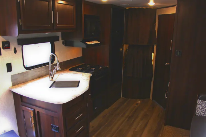 RV rental interior: dark wood kitchen, light countertop, sink, stovetop, microwave, and hallway visible.. Jayco Jay Flight SLX Rocky Mtn Edition 2019