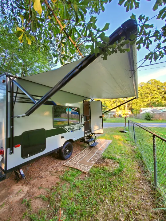 Small travel trailer RV rental with awning extended, door open, and steps down, parked under trees.. Forest River Salem 2020