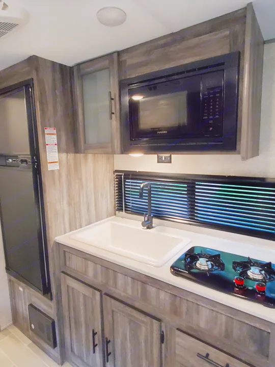 Modern RV rental kitchen featuring a refrigerator, microwave, sink, and stovetop, ready for your adventures.. Forest River Salem 2020