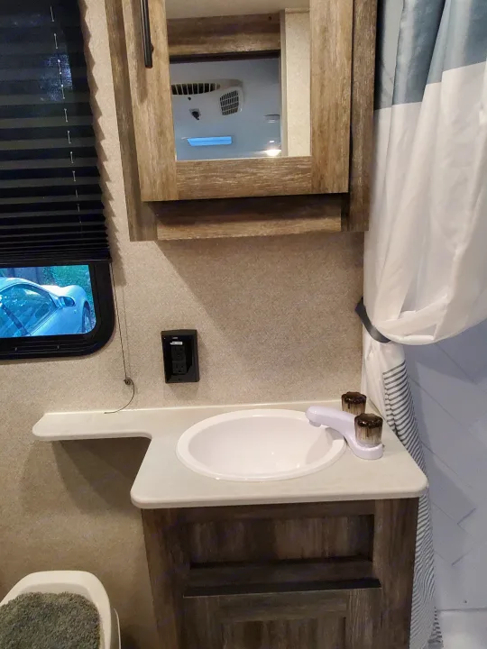 RV rental bathroom features a sink, mirror (reflecting AC), shower, and window with outdoor view. Compact & functional.. Forest River Salem 2020