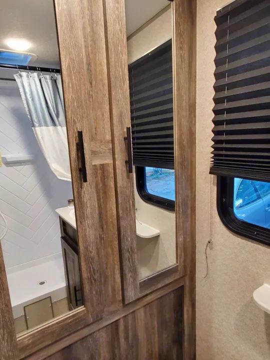 View inside an RV rental: a modern bathroom with shower and vanity, reflected in sleek wooden cabinet mirrors.. Forest River Salem 2020