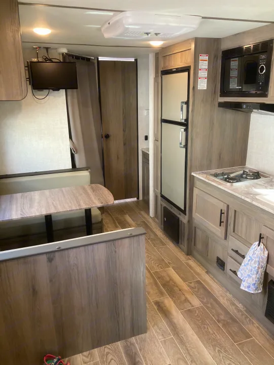 Cozy rv rental interior with modern wood-look finishes, featuring a kitchen, dinette seating, and wall-mounted TV.. Gulf Stream Conquest Lite 2021