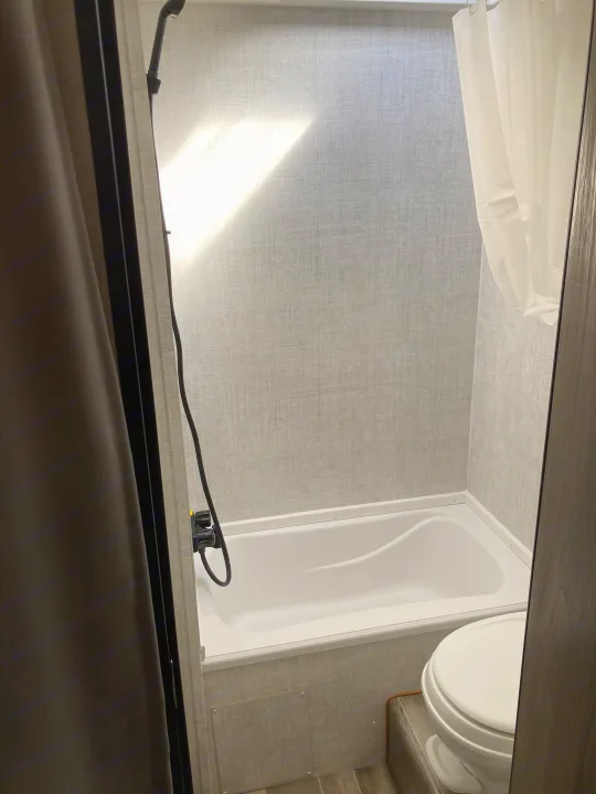 Compact RV rental bathroom featuring a shower/tub, toilet, textured walls, and natural light from above.. Gulf Stream Conquest Lite 2021