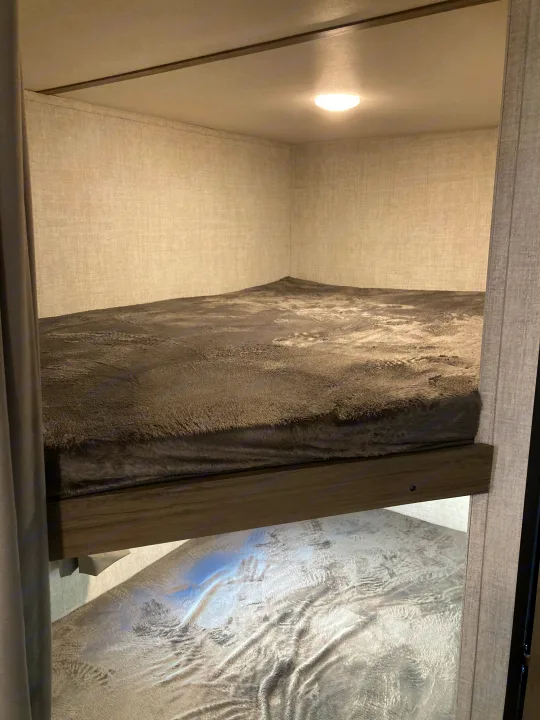 Cozy bunk beds inside an RV rental, with a dark fuzzy blanket on the top bunk and a lighter one on the bottom.. Gulf Stream Conquest Lite 2021