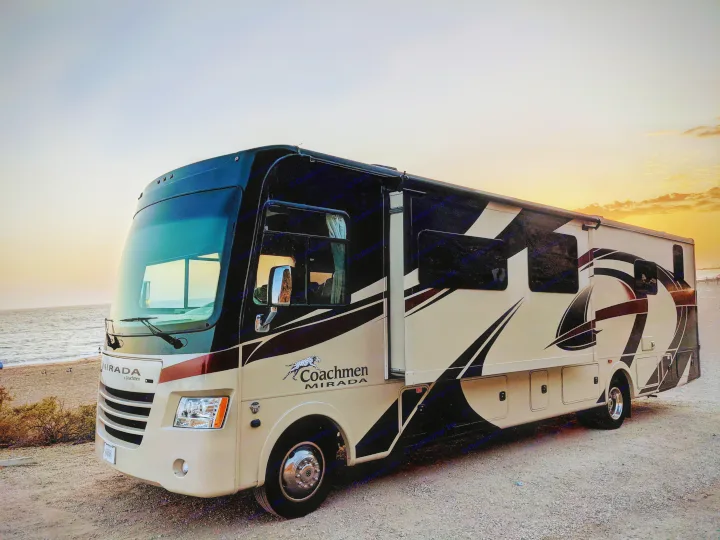 Sunset RV rental: A Coachmen Mirada motorhome parked on a gravel path by the ocean, with waves and glowing sky.. Coachmen Mirada 2019