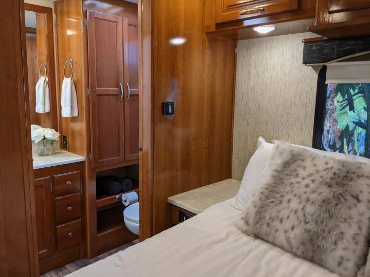 Cozy bedroom and compact bath area in a modern RV rental, featuring wood cabinetry and comfortable bedding.. Coachmen Mirada 2019