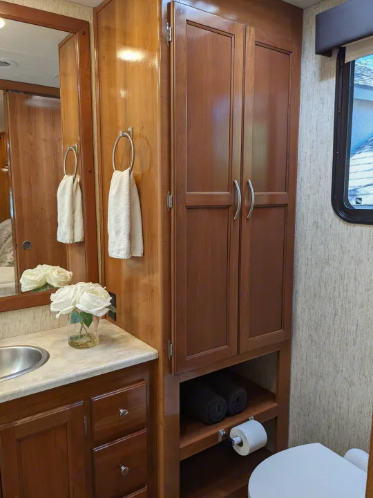 RV rental bathroom with wooden cabinets, sink, toilet, and white roses, showcasing a compact yet functional space.. Coachmen Mirada 2019