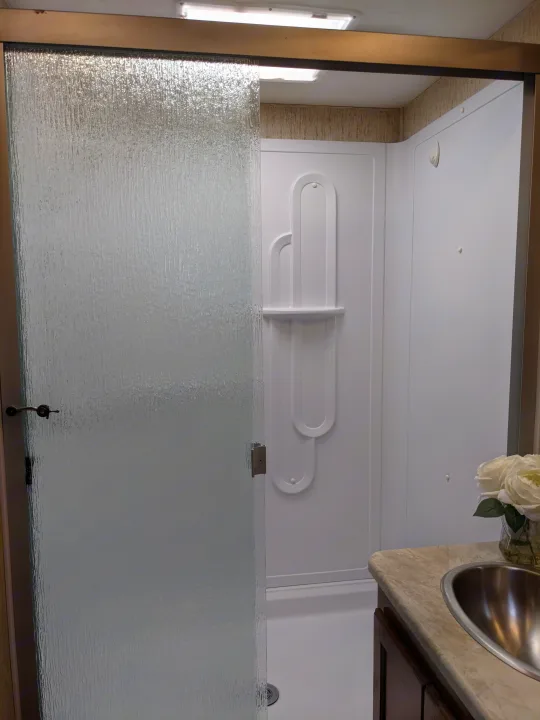 RV rental: Clean shower stall with textured glass door, integrated shelf, and adjacent vanity sink in the bathroom.. Coachmen Mirada 2019