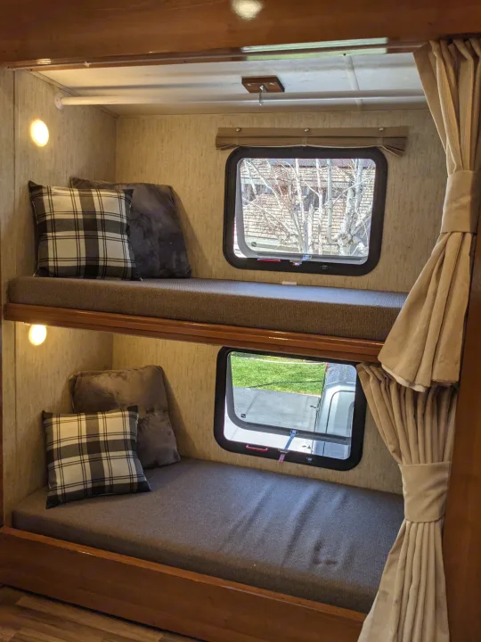 Explore this comfortable RV rental bunk bed area, featuring cozy mattresses, pillows, windows, and curtains for a pleasant journey.. Coachmen Mirada 2019