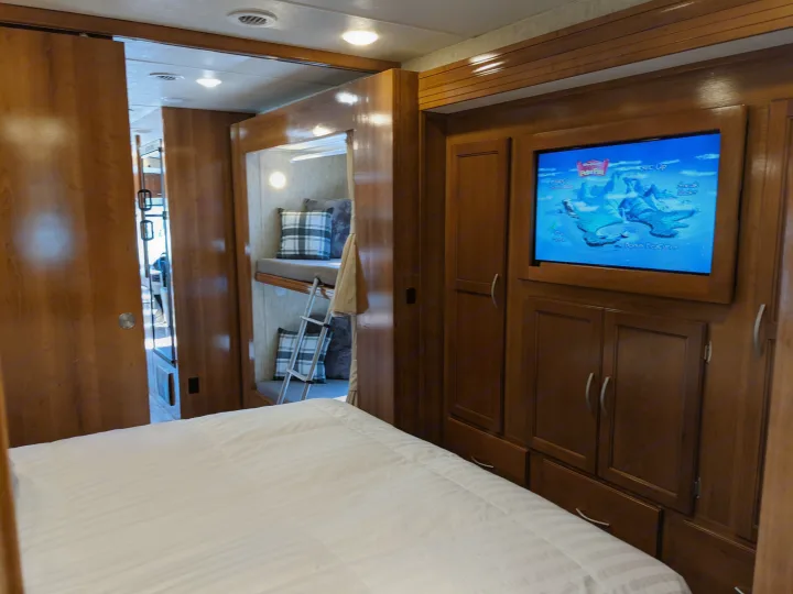 Cozy RV rental bedroom featuring a flat-screen TV, ample storage, and a peek into bunk beds through a wooden slider.. Coachmen Mirada 2019