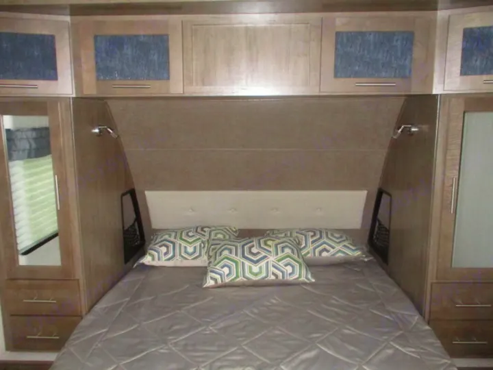 This RV rental bedroom features a cozy bed with pillows, overhead cabinets, and side wardrobes for storage.. Forest River Surveyor 2018