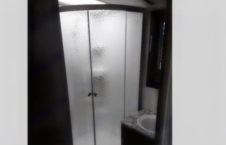 This RV rental features a compact bathroom with a curved frosted glass shower and a white sink on a granite-look counter.. Forest River Surveyor 2018