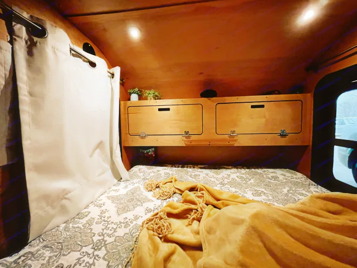 Cozy RV rental interior with a patterned bed, wood storage, bright lights, and window view, ideal for travel.. American Teardrop Travel Trailer 2016