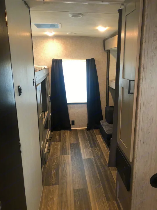 Cozy RV rental interior with a hallway leading to a bright window. Features bunk beds, laminate flooring, and overhead lights.. Heartland Mallard 2020