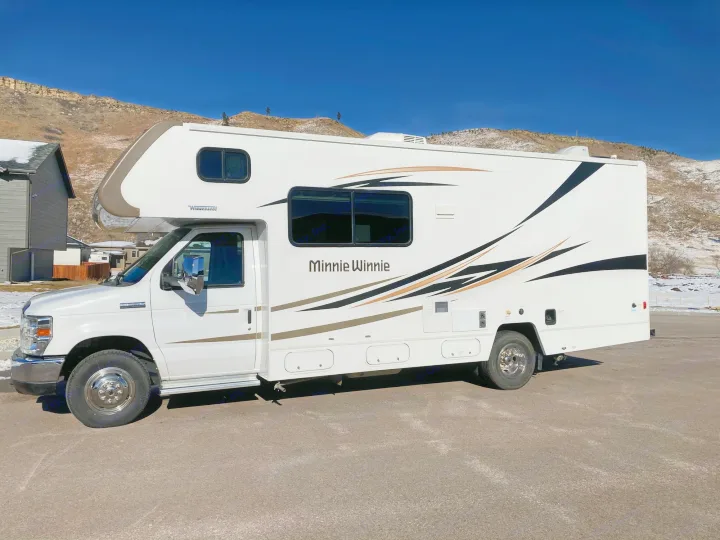 White Winnebago Minnie Winnie RV rental, a spacious Class C motorhome camper, parked on asphalt with scenic mountains.. Winnebago Minnie Winnie 2016