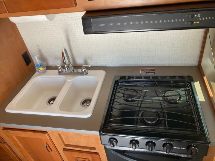 Clean RV rental kitchen interior: dual sink, Suburban stove/oven, and range hood, perfect for travel.. Winnebago Minnie Winnie 2016