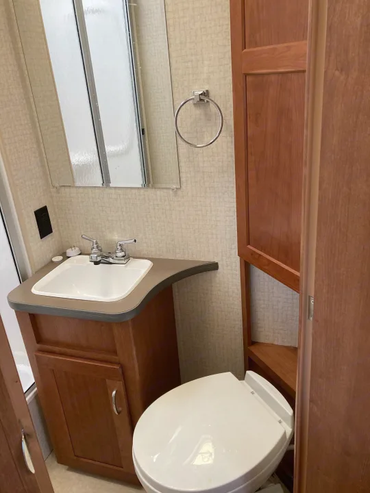 Functional RV rental bathroom with wood vanity, sink, toilet, and partially visible shower. Perfect for your travels.. Winnebago Minnie Winnie 2016