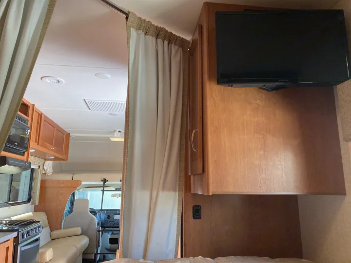 RV rental interior: Mounted TV, wood cabinets, and privacy curtain with a glimpse of the kitchen and cab beyond.. Winnebago Minnie Winnie 2016