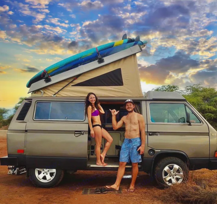 Adventure-ready! A couple with their pop-top VW campervan and surfboards at sunset. Your perfect RV rental.. VW Westfalia 1986