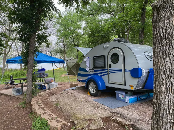 Teardrop camper at a serene lake campsite, ideal for your next rv rental adventure with blue canopy & gear.. Little Guy NuCamp 2015