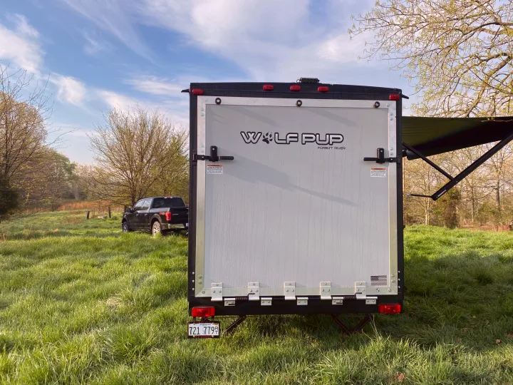 Rear view of a Wolf Pup travel trailer, great for RV rental adventures. Parked in a grassy field with a pickup truck and trees under a blue sky.. Forest River Wolf Pup 2021