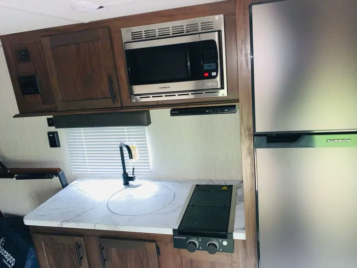Clean RV rental kitchen: Furrion fridge, Contoure microwave, Greystone stovetop, sink, and stylish marble-look counters.. Forest River Wolf Pup 2021