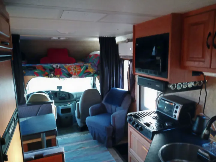 Comfy RV rental interior: well-equipped kitchen (stove, microwave, sink), dinette, living area, and cab-over bed visible.. Four Winds Majestic 2009