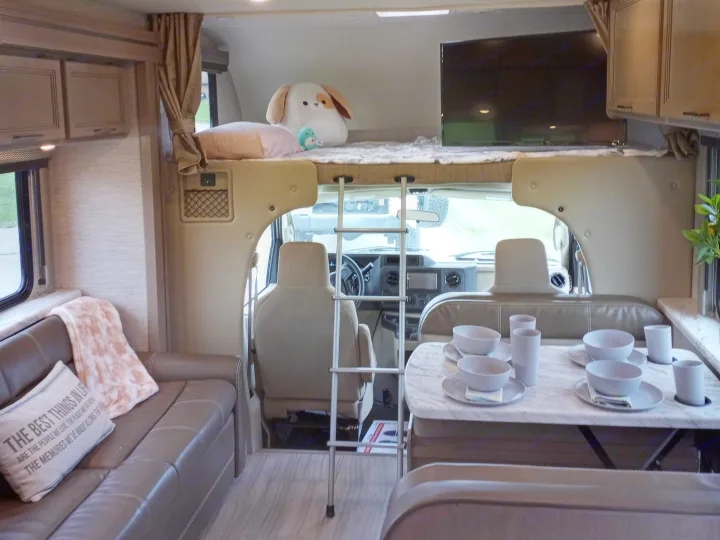 Inside a comfortable RV rental, featuring a front bunk bed, dining area, and plush sofa. Ready for travel.. Coleman Thor 2021