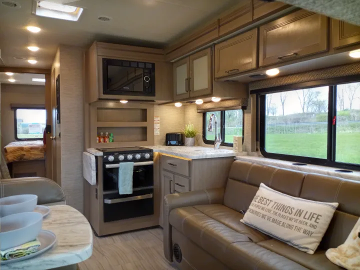 Cozy RV rental interior showing a well-equipped kitchen with microwave & stove, a living area with sofa, and a bedroom.. Coleman Thor 2021