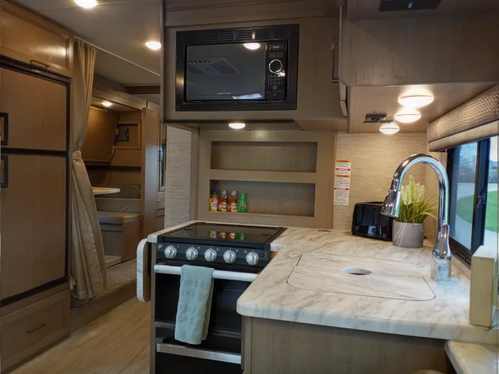 Modern RV rental interior showcasing a full kitchen with microwave, stove, sink, and refrigerator, ideal for comfortable travel.. Coleman Thor 2021