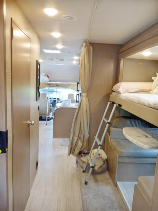 Interior of an rv rental: hallway leading to bunk beds with a ladder, a dog in a bed, and a dining area visible.. Coleman Thor 2021
