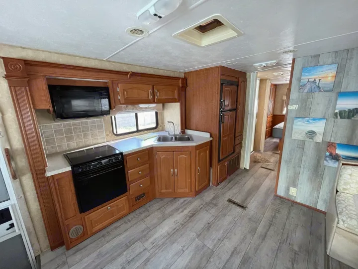 RV rental interior showcasing a full kitchen with wood cabinetry, black appliances, and modern gray flooring.. Forest River Georgetown 2007