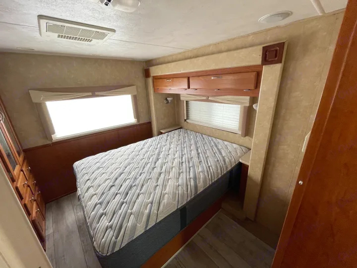 Spacious RV rental bedroom featuring a comfortable queen bed, overhead cabinets, and bright windows.. Forest River Georgetown 2007