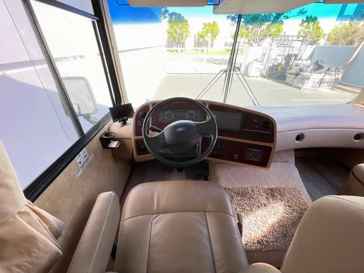 Explore the open road! Clean RV rental cockpit with driver's view of dashboard, steering wheel, and spacious front window.. Forest River Georgetown 2007