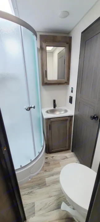 RV rental bathroom features a curved glass shower, vanity with sink, and toilet, designed for travel comfort.. Venture Rv Sporttrek 2021