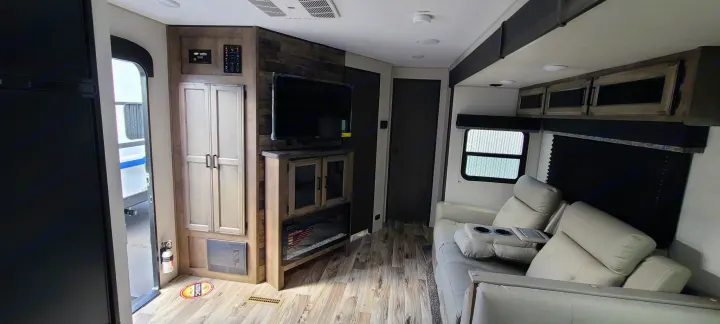 The interior of an RV rental, showing a cozy living space with light-colored recliners, a mounted TV, and wood-paneled walls.. Venture Rv Sporttrek 2021