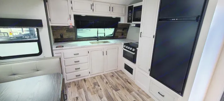 Spacious RV rental kitchen with modern white cabinets, appliances (fridge, stove, microwave), and a dining booth.. Venture Rv Sporttrek 2021